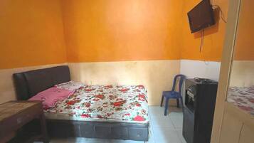 Une petite chambre à coucher composée d’une seule pièce, comprenant un lit, un bureau, une chaise et un téléviseur.