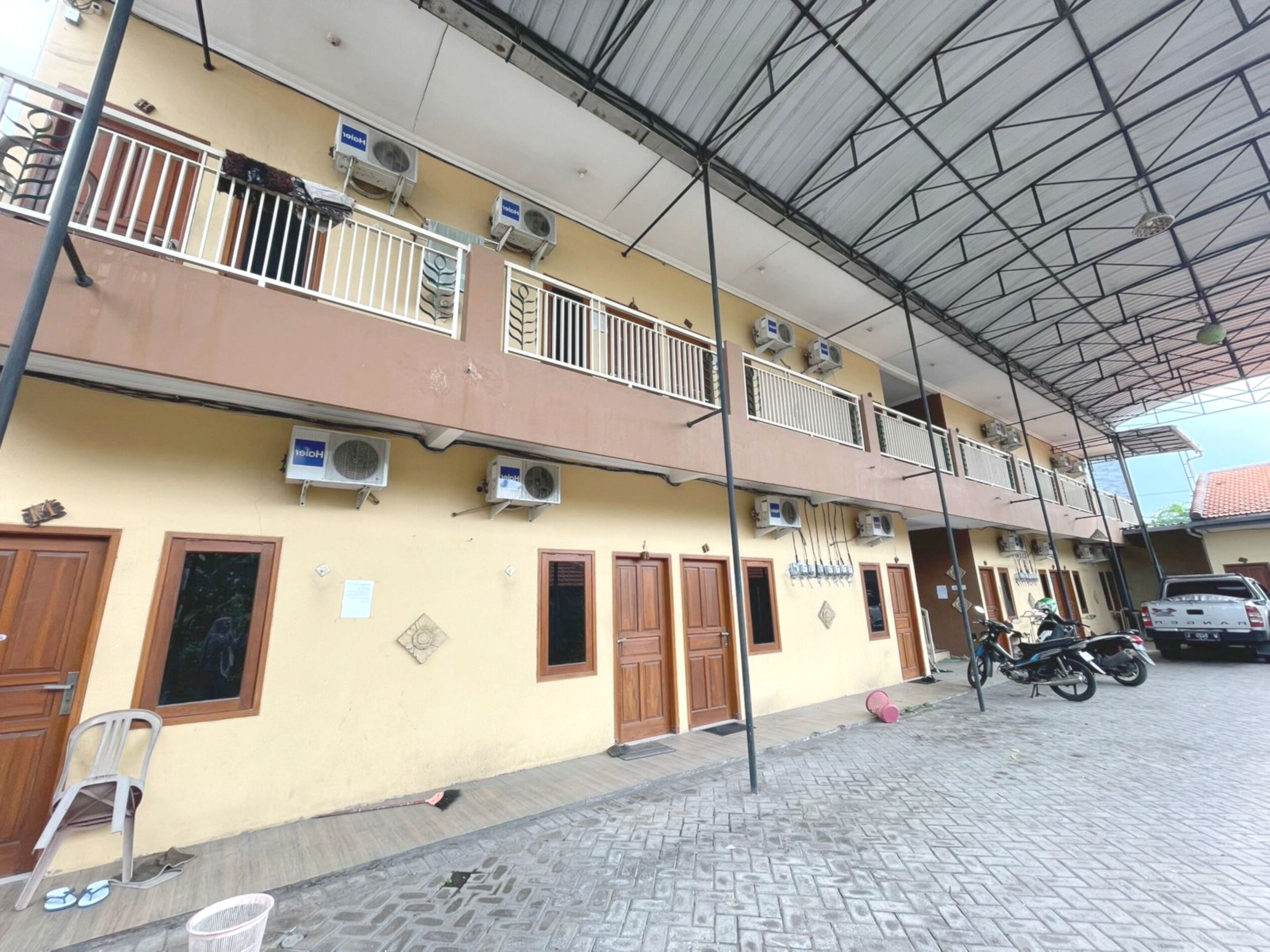 A two-story building with multiple air conditioning units, a covered outdoor area, and a parked motorcycle.