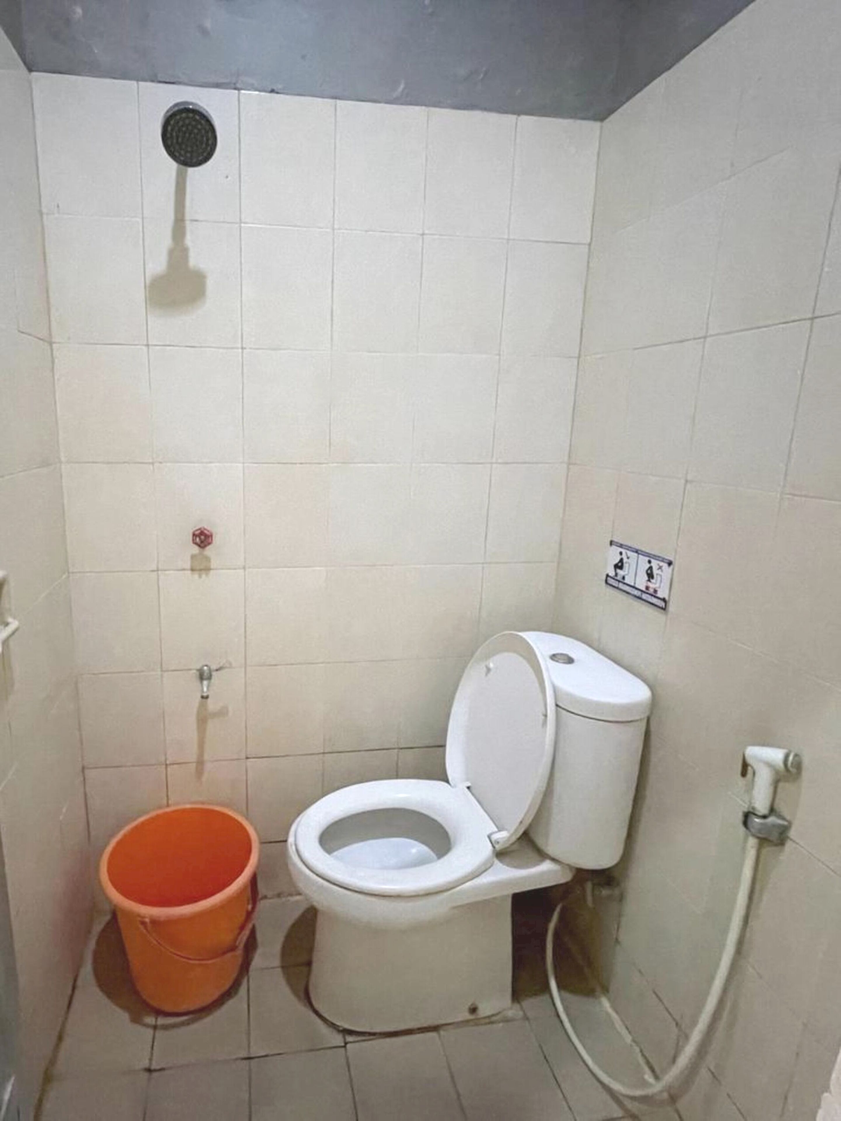 A small, tiled bathroom with a toilet, a showerhead, and a bucket.