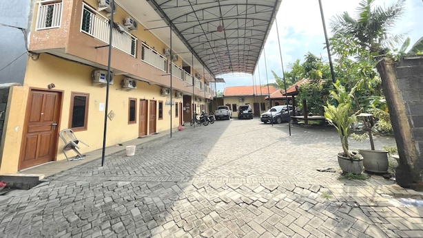 A courtyard with a covered walkway, a building with multiple balconies, and parked cars. - Hotel O Hidayah Homestay Syariah (Sidoarjo)