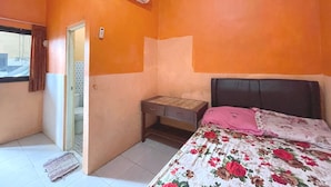 A bedroom with an orange wall, a bed with floral bedding, a desk, and an air conditioner. - Hotel O Hidayah Homestay Syariah (Sidoarjo)