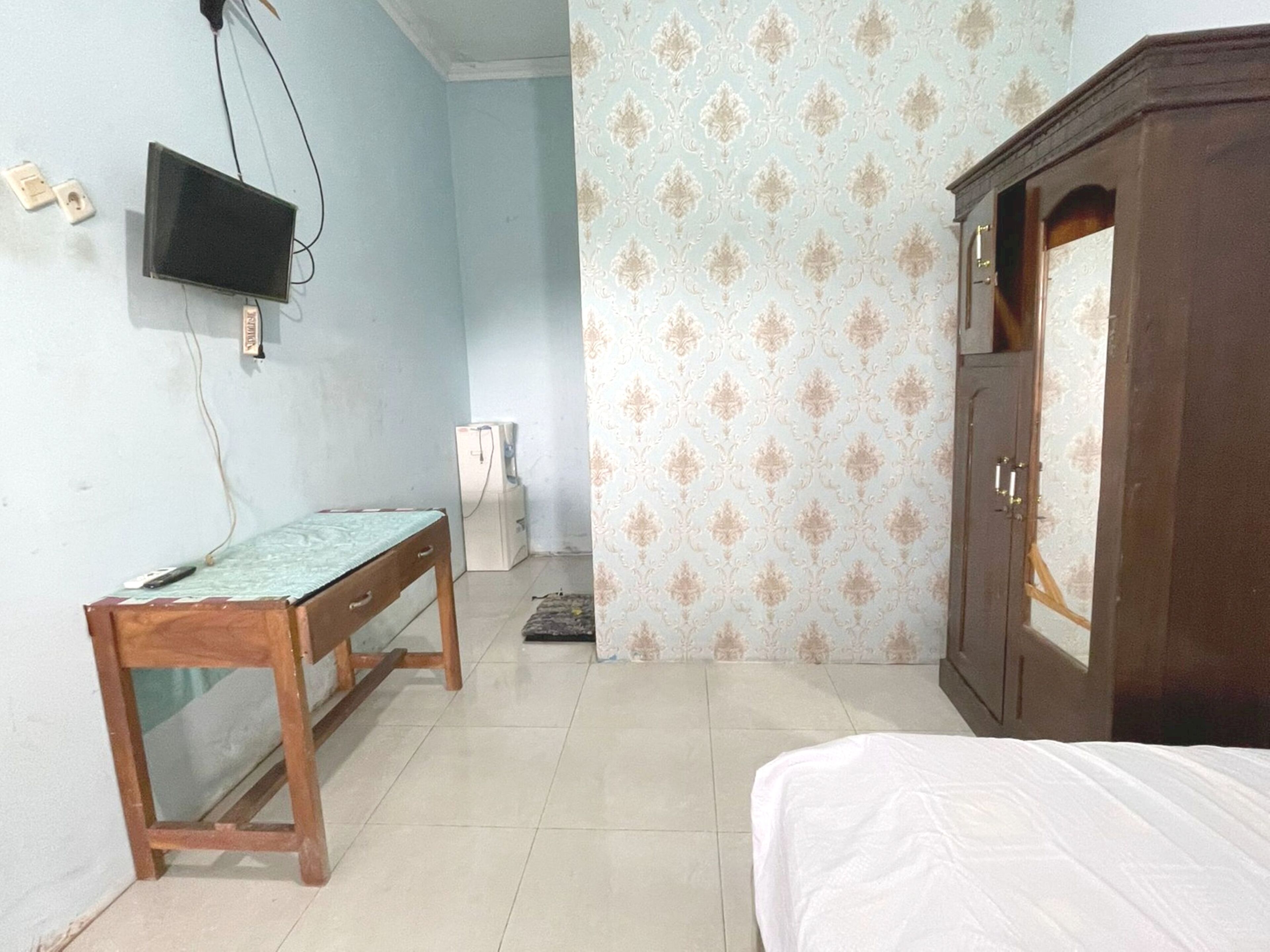 A room with a bed, a wooden desk, a television mounted on the wall, and a wardrobe.