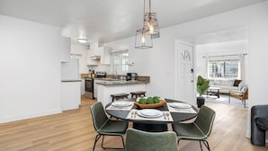 Una cocina moderna con armarios blancos, un comedor con una mesa redonda y una sala de estar con sofá y mesa de centro.