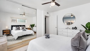 Un dormitorio moderno con una cama grande, un ventilador de techo, un espejo redondo y una mesita de noche con una lámpara.