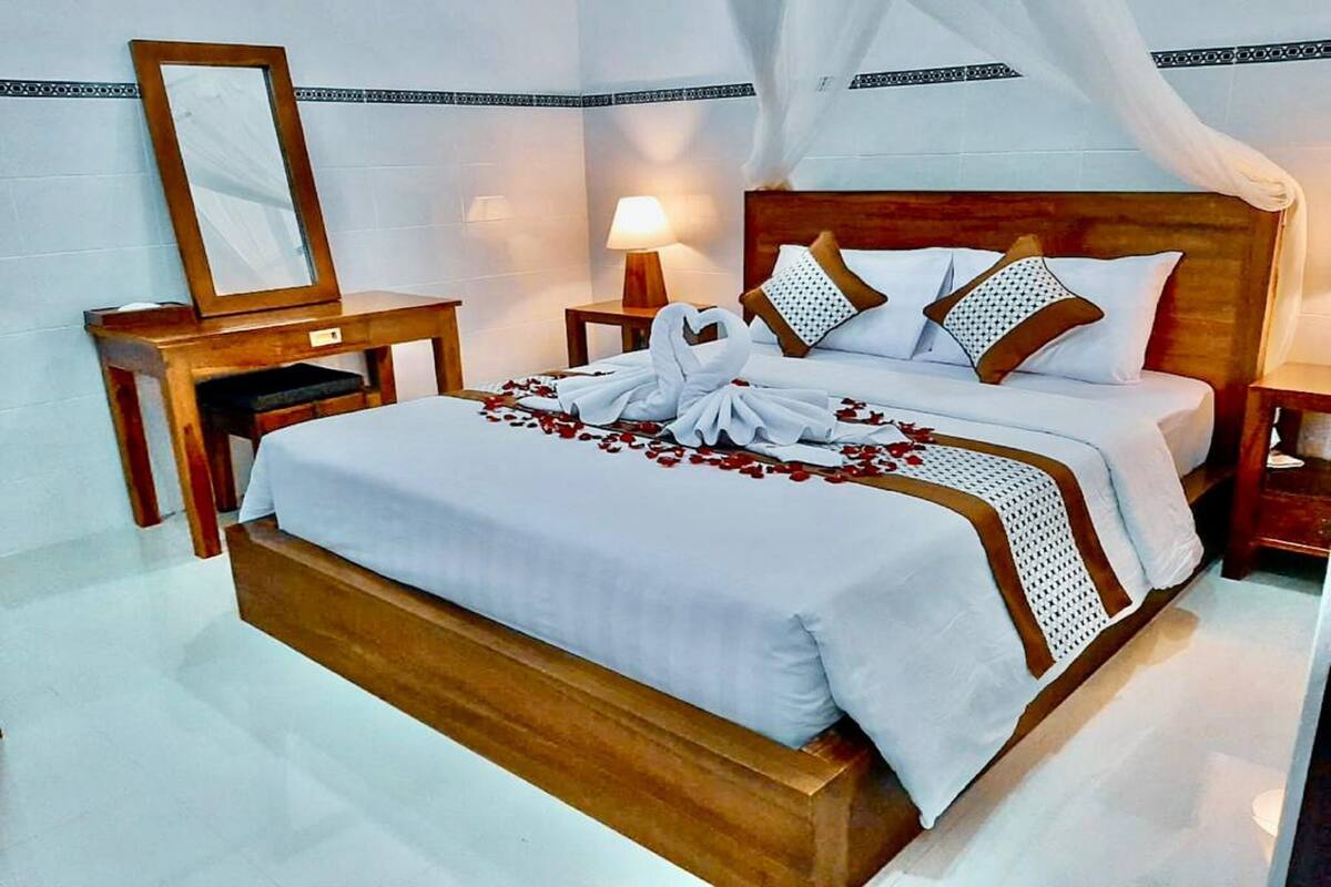 Un lit bien fait, avec du linge de lit blanc et une tête de lit en bois, une table de chevet avec une lampe et un miroir accroché au mur.