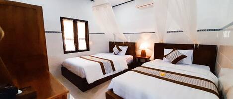 Ein Hotelzimmer mit zwei Betten, einem Holfnachtkästchen, einem Beistelltisch und einem Fenster mit Vorhängen.