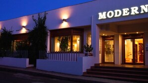 Une entrée d'hôtel moderne, avec une enseigne bien visible portant l'inscription « MODERNO », des marches menant à la porte et un éclairage extérieur.