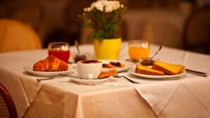 Une table dressée pour le petit-déjeuner, avec des croissants, une tasse de café, du jus d’orange et une assiette de fromage.
