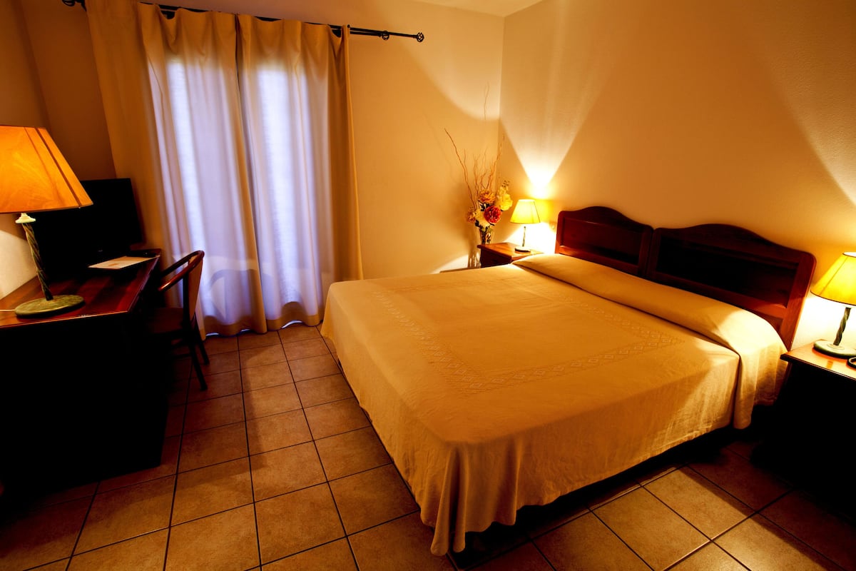 A hotel room with a bed, a desk with a chair, a TV, and a lamp.