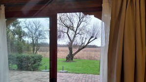 Blick durch eine Glastür auf eine Pflasterterrasse, einen Baum und eine Wiese.