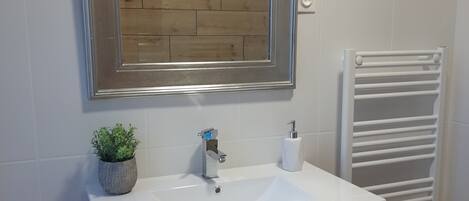A bathroom with a wooden vanity, a white sink, a mirror, and a towel rack.