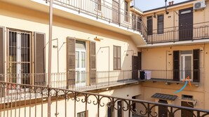 Un edificio de varios pisos con balcones, barandillas de metal y un patio empedrado.