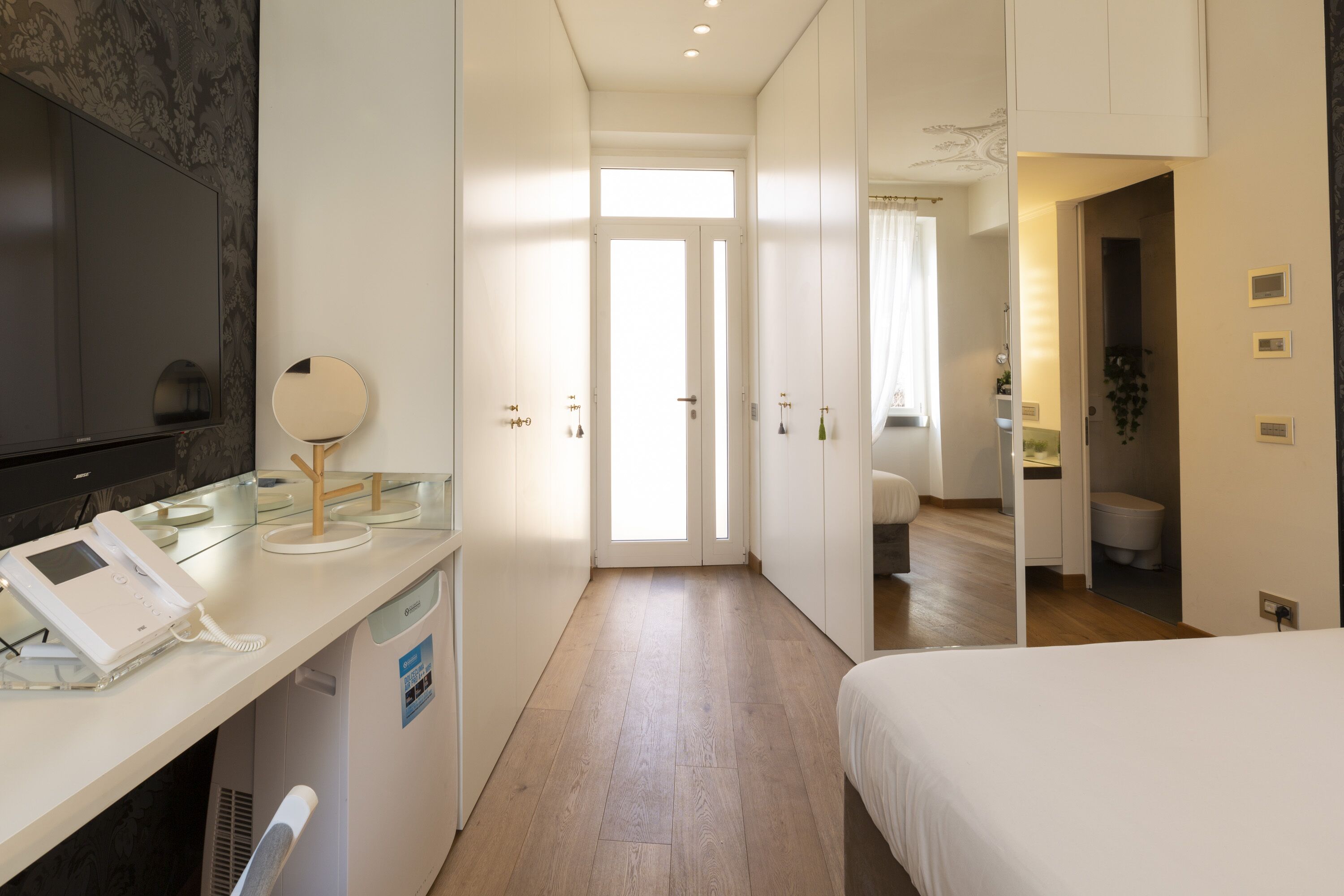 Une chambre d’hôtel avec un lit, un bureau avec un téléphone, un miroir et une télévision. Une porte donne accès à la salle de bain.