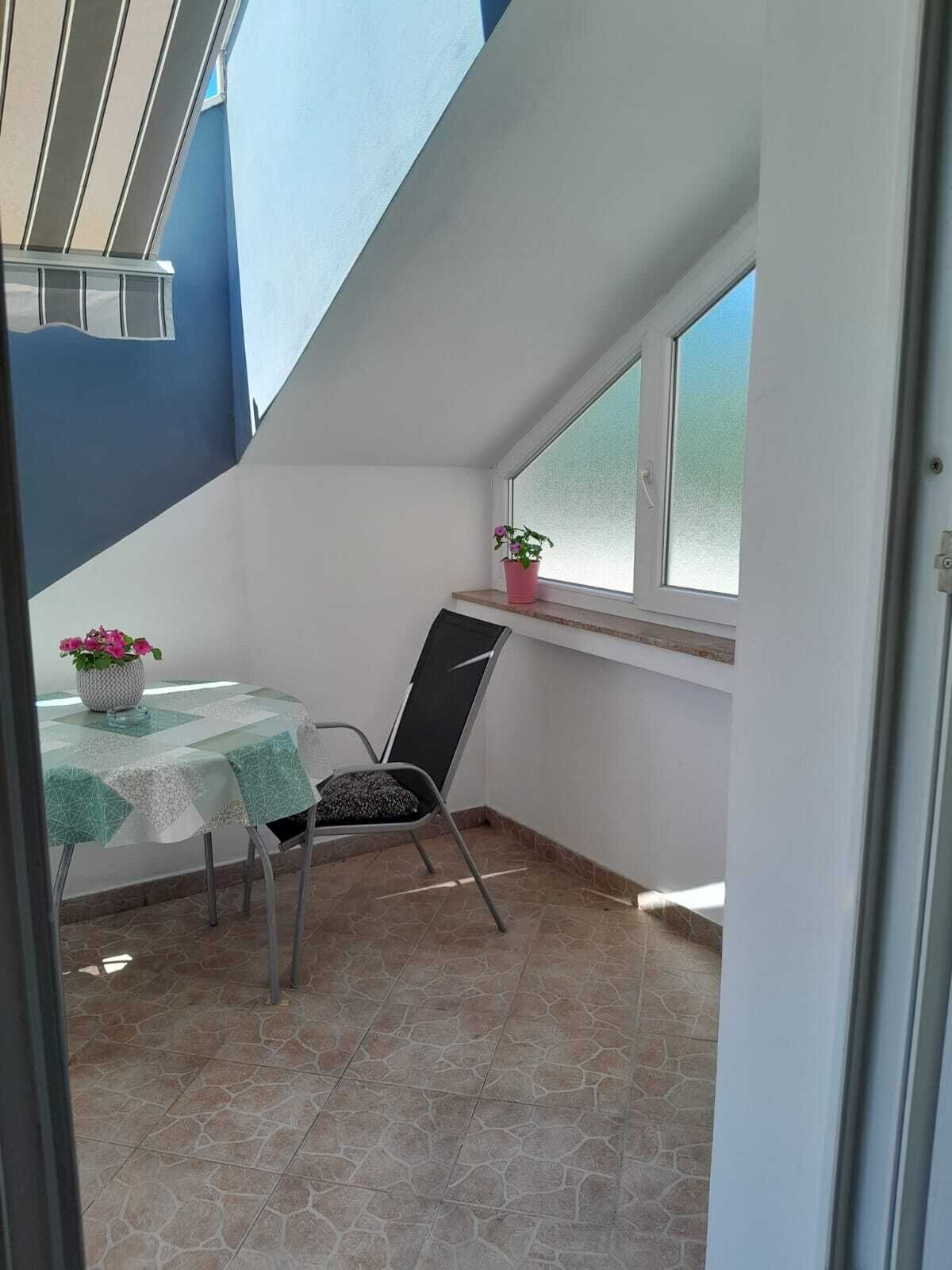 Een klein zitehoekje met een tafel en stoel, een plant in pot en een raam met uitzicht.