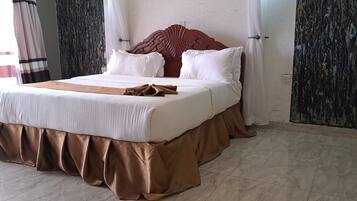 Una cama bien tendida con cabecera de madera, ropa blanca y falda marrón.