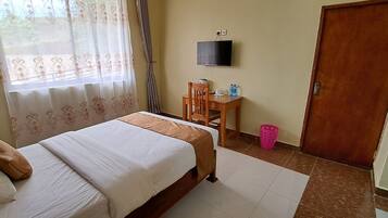 Quarto de hotel com uma cama, uma escrivaninha com cadeira, uma televisão na parede e uma porta.