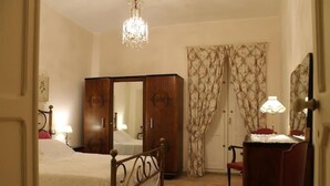 Een slaapkamer met een bed, een kledingkast, een bureau met stoel, een kroonluchter en gordijnen.