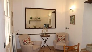 Een woonkamer met twee fauteuils, een kleine ronde tafel, een spiegel en een schilderij aan de muur.