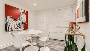 A modern dining area with a white round table and chairs, a zebra painting on the wall, and a plant on a stand. - Hilltop I Cherry Creek I Guest suite I Museums (Denver)