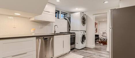 A modern kitchen with white cabinetry, stainless steel appliances, and a built-in washer and dryer.