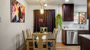 A dining area with a wooden table and chairs, a modern kitchen with stainless steel appliances, and a colorful abstract painting on the wall. - Insta-Worthy 5BR Home I Pet Friendly  I Firepit (Denver)