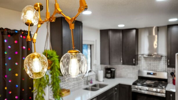 A modern kitchen with dark cabinets, a stainless steel stove, and a hanging light fixture with clear glass globes. - Insta-Worthy 5BR Home I Pet Friendly  I Firepit (Denver)