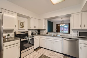 A modern kitchen with white cabinetry, a built-in oven, a microwave, and a window with a view of greenery.