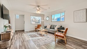 A spacious living room with hardwood flooring, a ceiling fan, a sofa, a coffee table, and a TV.