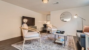 A modern living room with a flat-screen TV, two chairs, a coffee table, and a sofa.