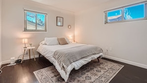 A bedroom with a bed, bedside lamps, a rug, and two windows with views.