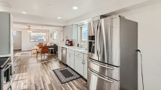 A modern kitchen with stainless steel appliances, a dining area with a wooden table and chairs, and a view of the outdoors through the window.
