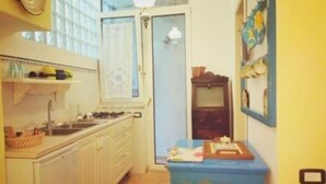 A narrow kitchen with white cabinets, a sink, and a stove. There is a blue table with a few items on it. - Cilento Antico Holiday Homes a few km from the sea (Stella Cilento)