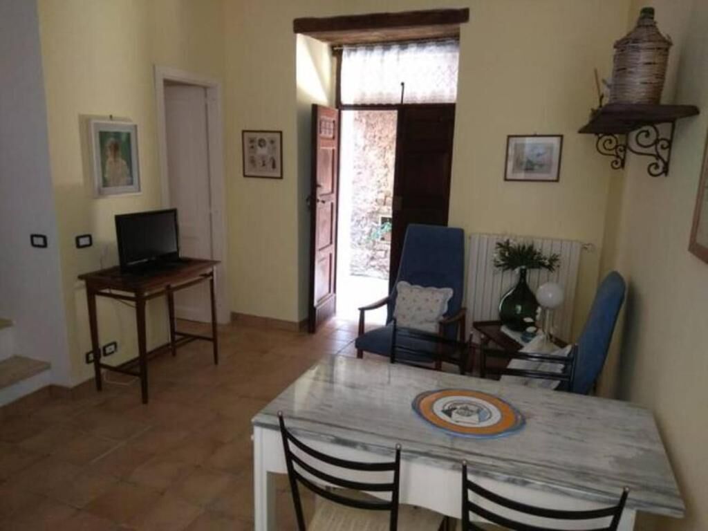 A dining area with a marble table, two chairs, a blue armchair, and a television on a wooden table.