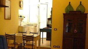 A dining area with a table and chairs, a kitchen in the background, and a cabinet with glass doors. - Cilento Antico Holiday Homes a few km from the sea (Stella Cilento)