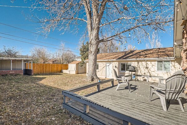 A backyard with a wooden deck, a barbecue grill, and a covered patio area.