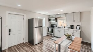 A modern kitchen with stainless steel appliances, white cabinetry, and a wooden dining table.