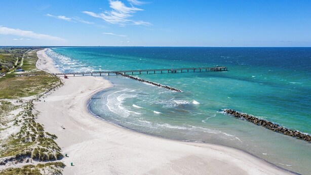 A beach with a wooden pier extending into the ocean, surrounded by clear blue waters and sandy shores. - Appartement Himmelblau mit Blick auf Bodden und Ostsee im Ostseebad Wustrow (Wustrow)