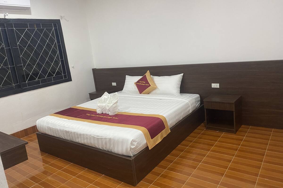 A neatly made bed with a white and maroon bedspread, two pillows, and a folded white towel on the bed.