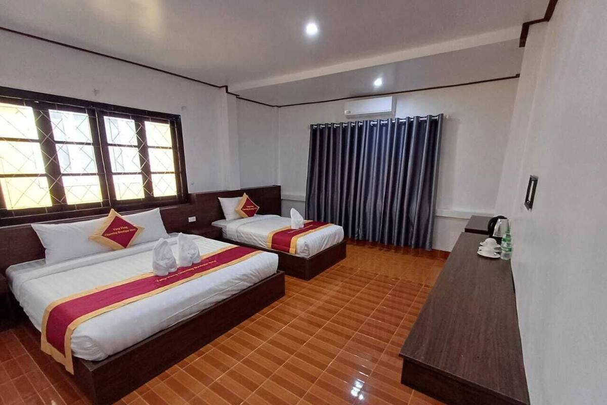 A hotel room with two beds, a wooden floor, a desk, and a window with curtains.