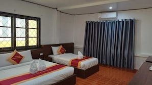 Een hotelkamer met twee bedden, een houten vloer, een raam met uitzicht en een gordijn.
