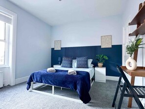 Une chambre à coucher avec un lit, des tables de chevet, une chaise, une plante et des œuvres d’art accrochées aux murs.