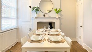 A dining room with a white table set for six, a fireplace, and two potted plants on the mantel. - Spacious & stylish 3-bed home in Centre of Canterbury (Canterbury)