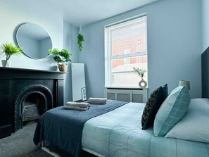 Un dormitorio con cama, chimenea, espejo y ventana con persianas.