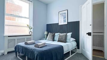 Une chambre à coucher avec un lit, une table de chevet, une lampe, une fenêtre avec des stores et une porte.