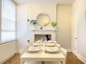 A dining room with a white table set for six, a fireplace, and a mirror on the wall.