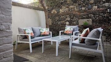 A patio area with two white sofas and a small table, set against a stone wall.