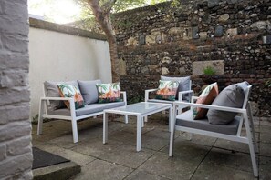 Eine Terrassenfläche mit zwei weißen Sofas und einem kleinen Tisch, vor einer Steinwand.