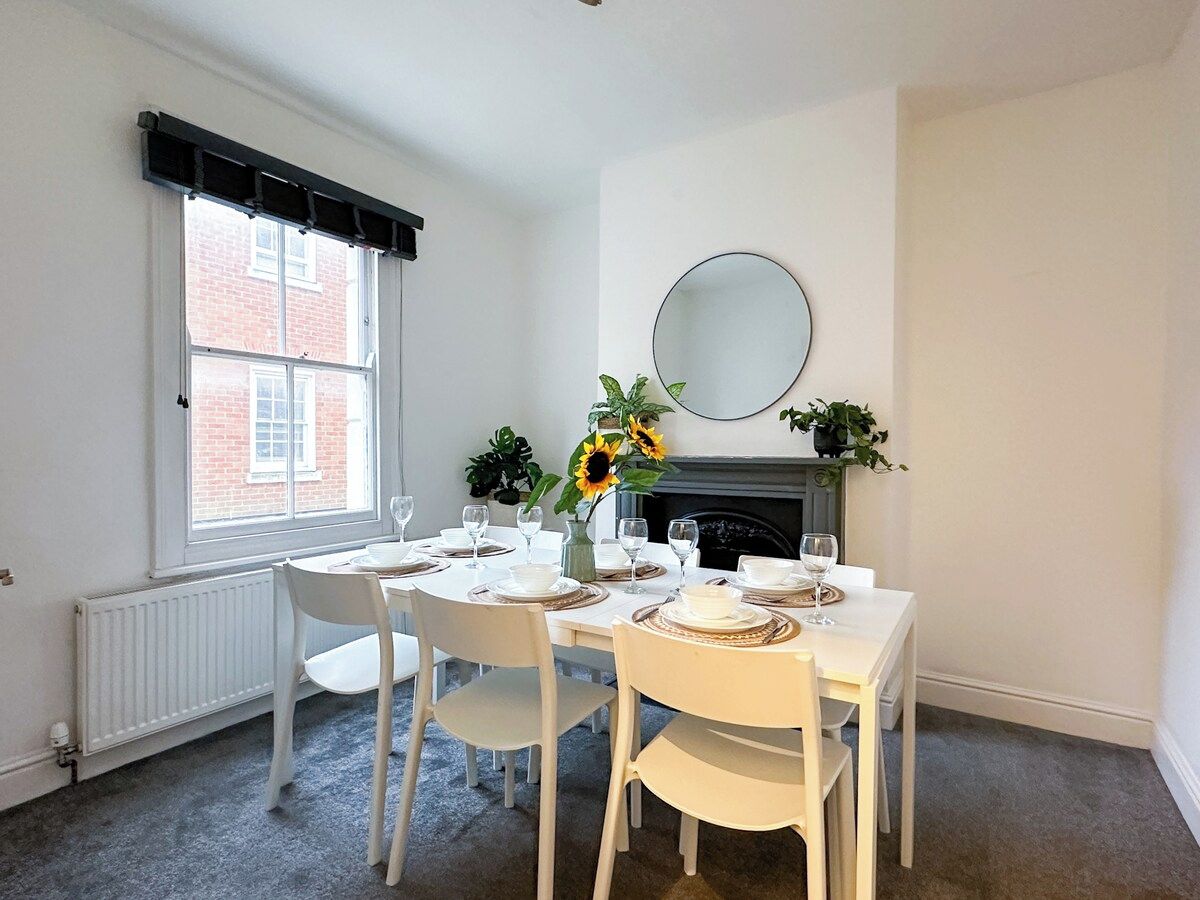 A dining area with a table set for four, a fireplace, and a window with blinds.