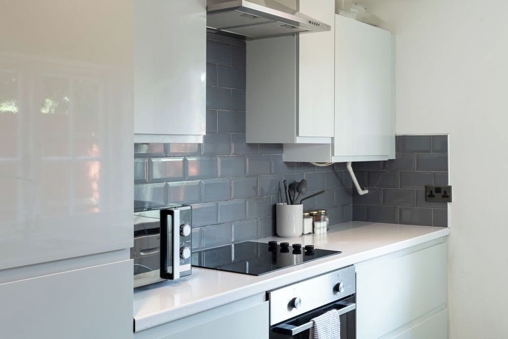 A modern kitchen with white cabinetry, a built-in stove, and a tiled backsplash.