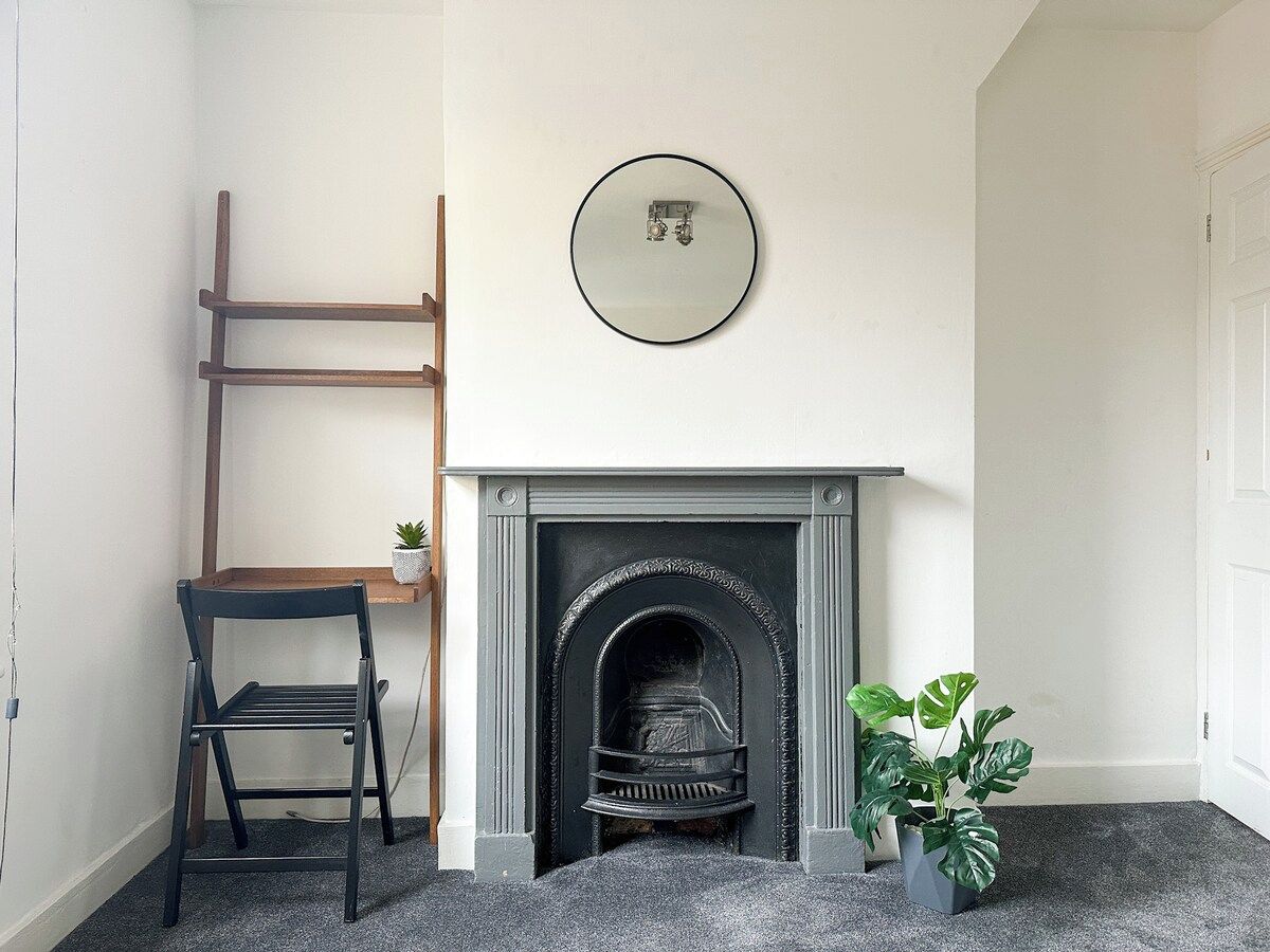 A room with a fireplace, a chair, a ladder, and a potted plant.
